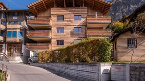 Un edificio de madera de varios pisos con balcones, un muro de piedra y montañas al fondo.