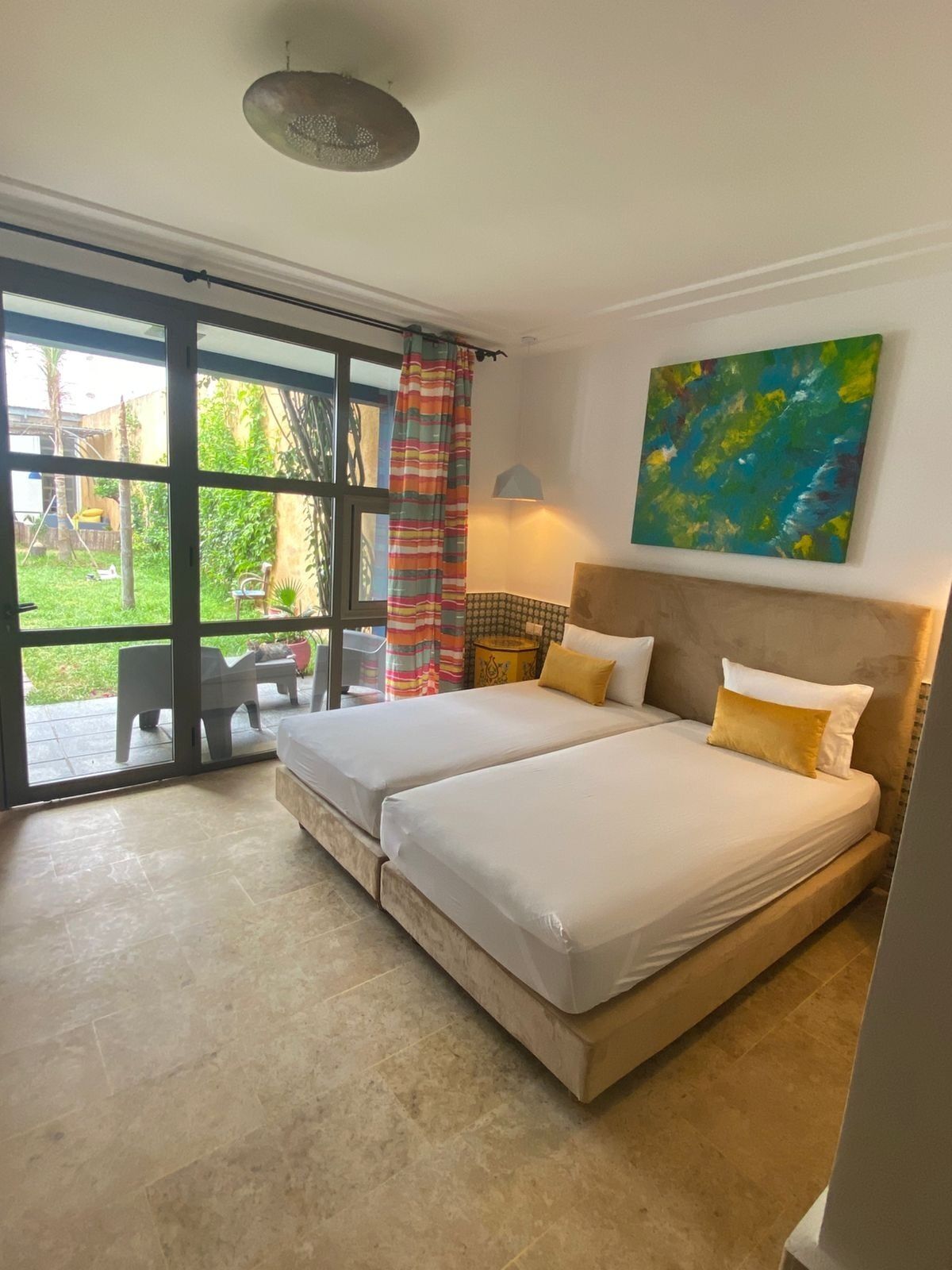 Un dormitorio con dos camas, un ventanal grande, un ventilador de techo y un cuadro en la pared.