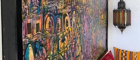 Un gran cuadro abstracto en una pared, un sofá estampado y un farol que cuelga de la pared.