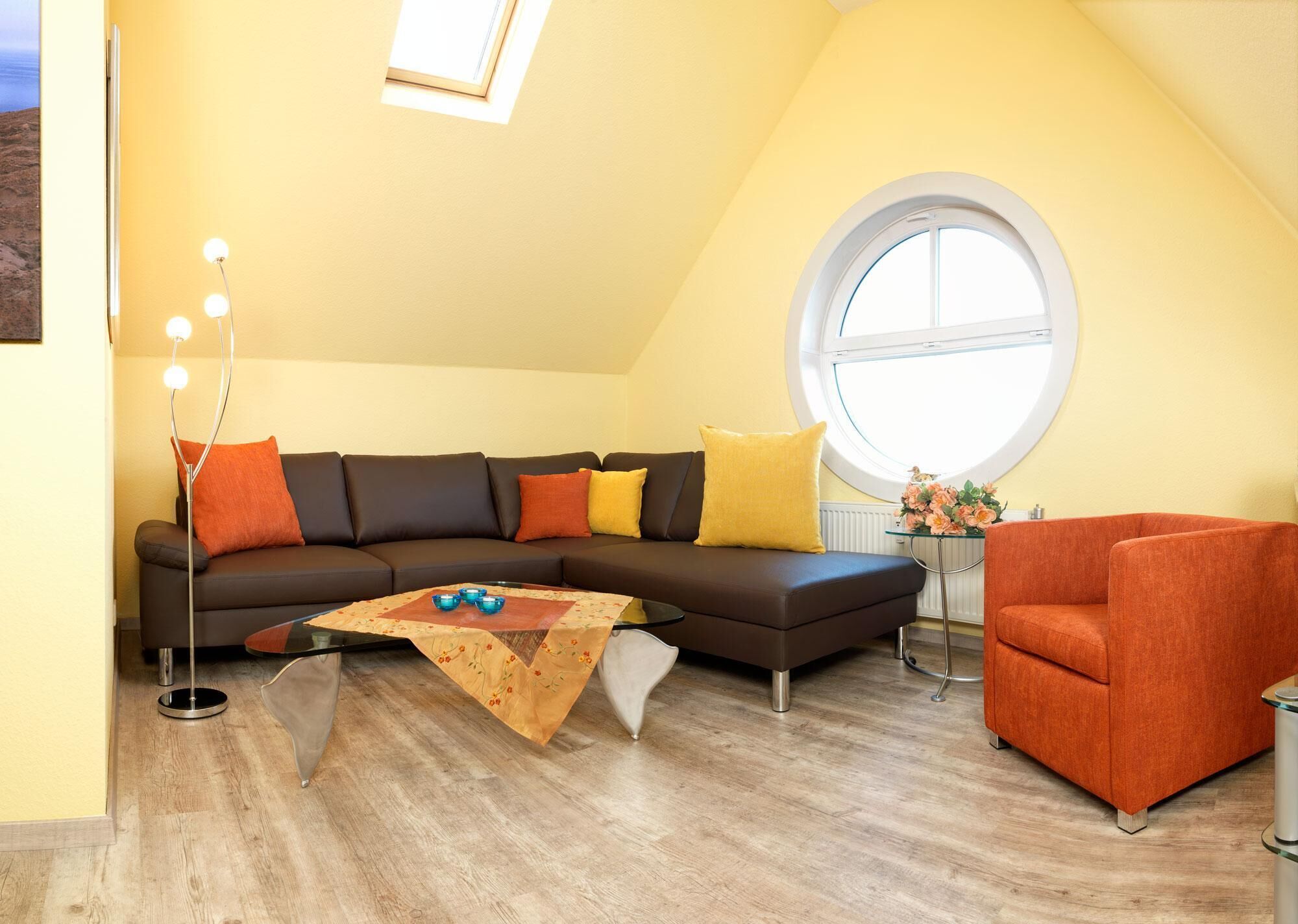 A modern living room with a sectional sofa, a glass coffee table, a round table with flowers, and a large window.
