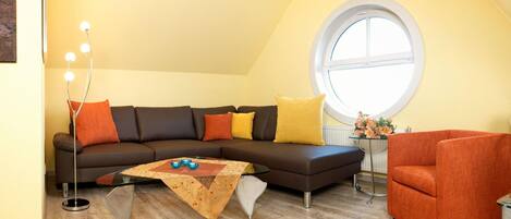 A modern living room with a sectional sofa, a glass coffee table, a round table with flowers, and a large window.