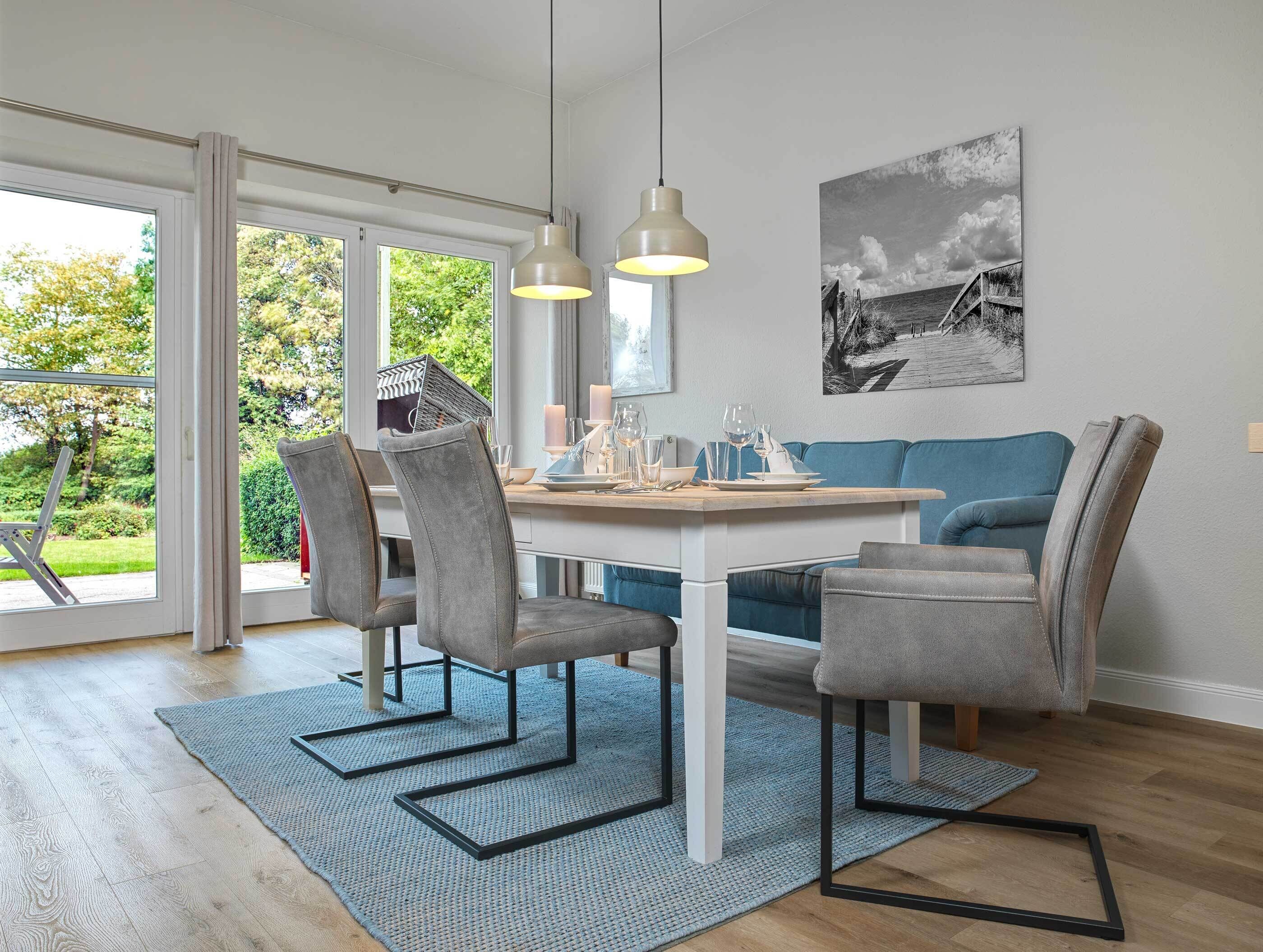 A dining area with a table set for four, grey upholstered chairs, a blue sofa, and a black and white landscape painting on the wall.