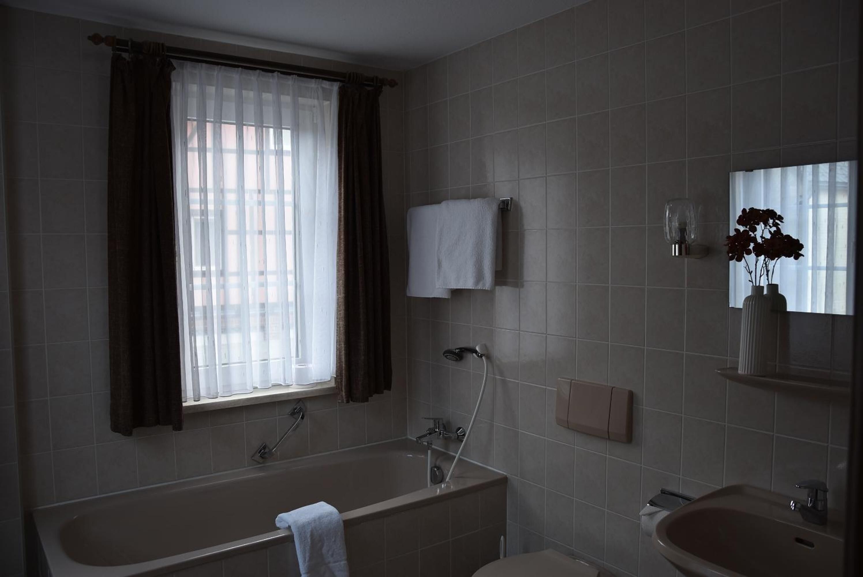 A bathroom with a bathtub, a sink, a window with curtains, and a mirror.