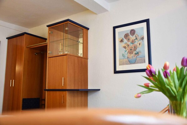 A wooden cabinet with a glass top, a framed painting of flowers, and a vase with tulips. - Landhotel Zum Hirsch (Unterweißbach)