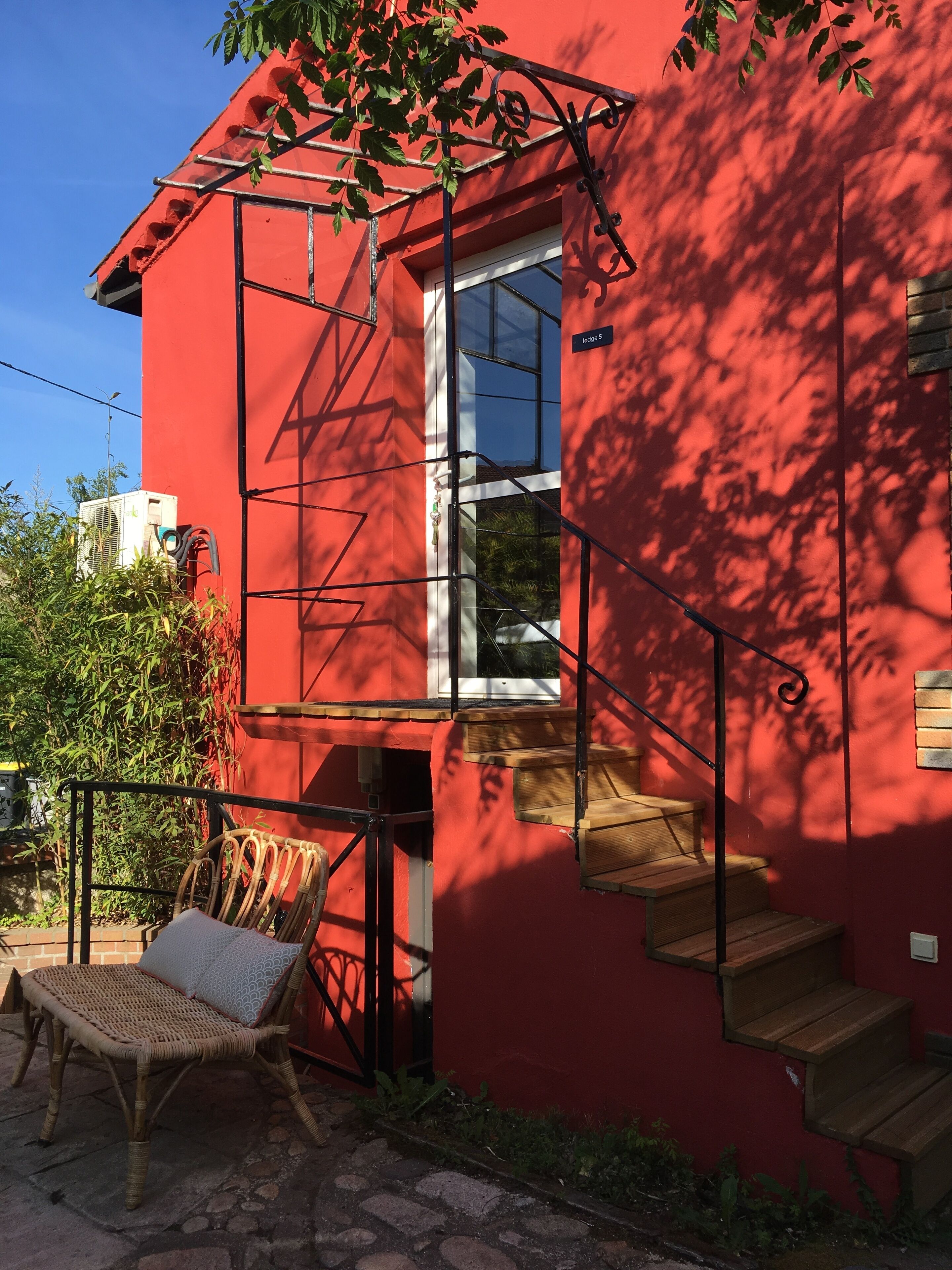 A red building with a window, a wooden staircase, and a wicker chair outside.