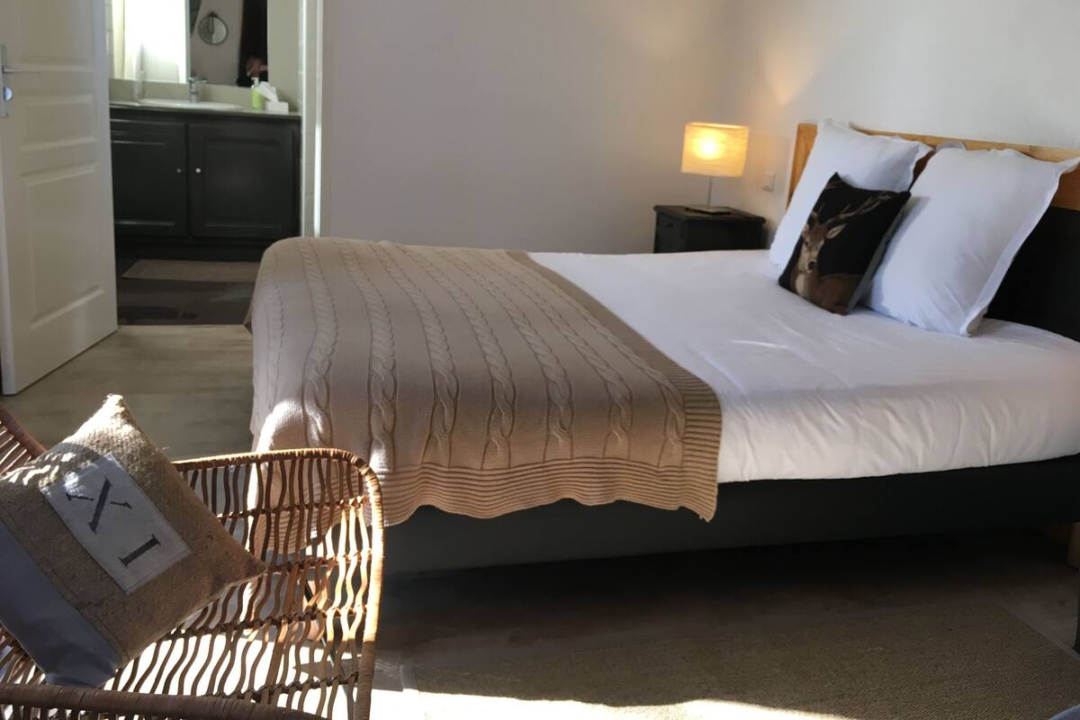 A bedroom with a bed, bedside table, lamp, and a wicker chair.