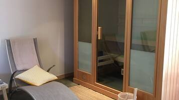 Een moderne kamer met een houten garderobe, een fauteuil, een klein tafeltje en een geweven vloermat.