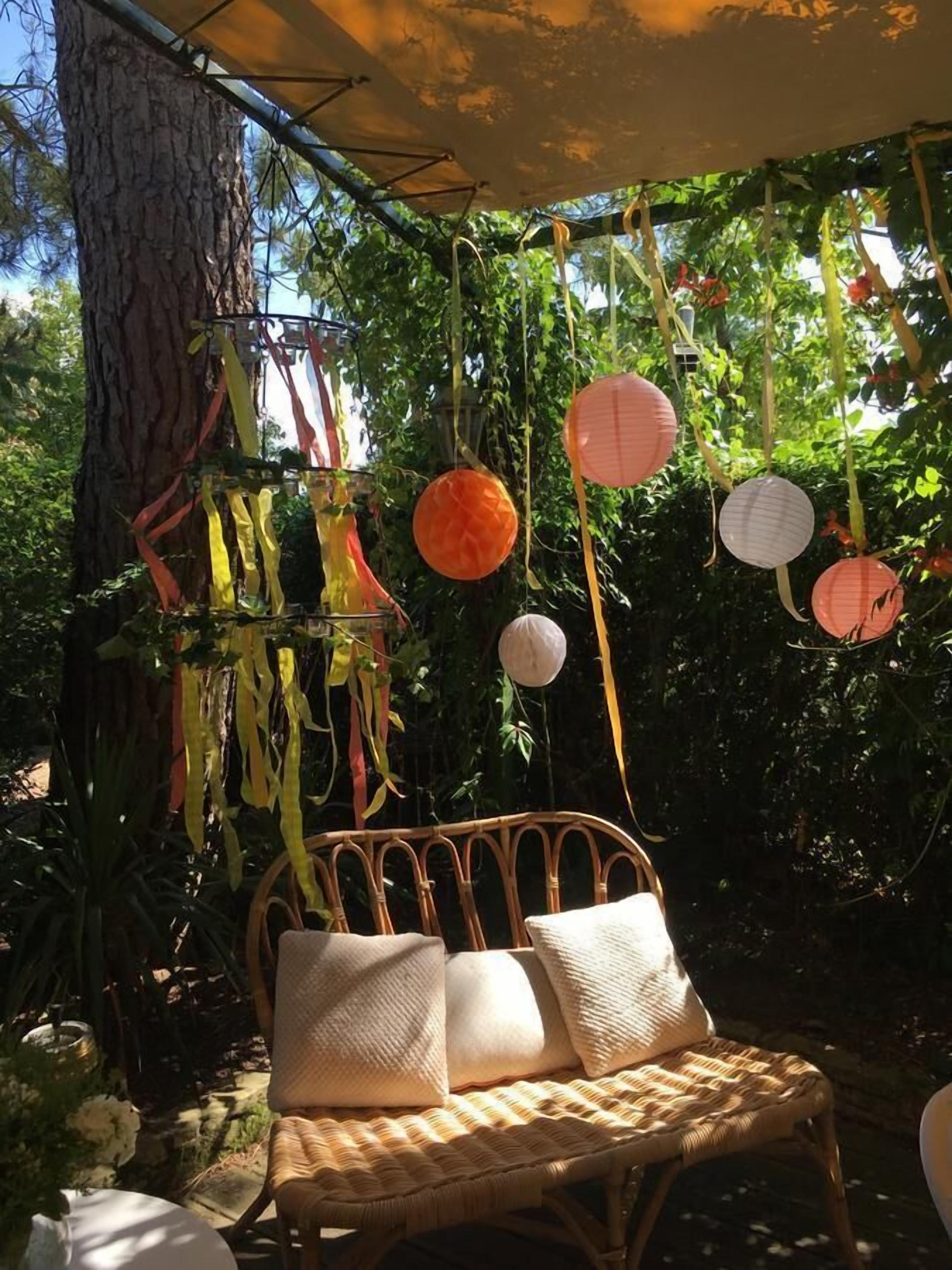 A wicker chair with cushions under a canopy, surrounded by hanging decorations and greenery.