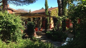 Um jardim com pérgola, área de estar ao ar livre e um edifício vermelho ao fundo.
