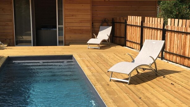 Um deck de madeira com piscina e duas cadeiras de descanso.