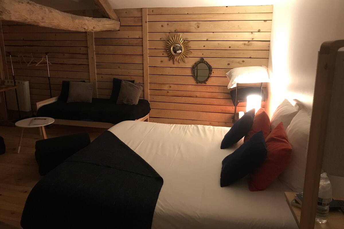 A cozy room with a bed, a sofa, a small table, and a wall-mounted mirror.