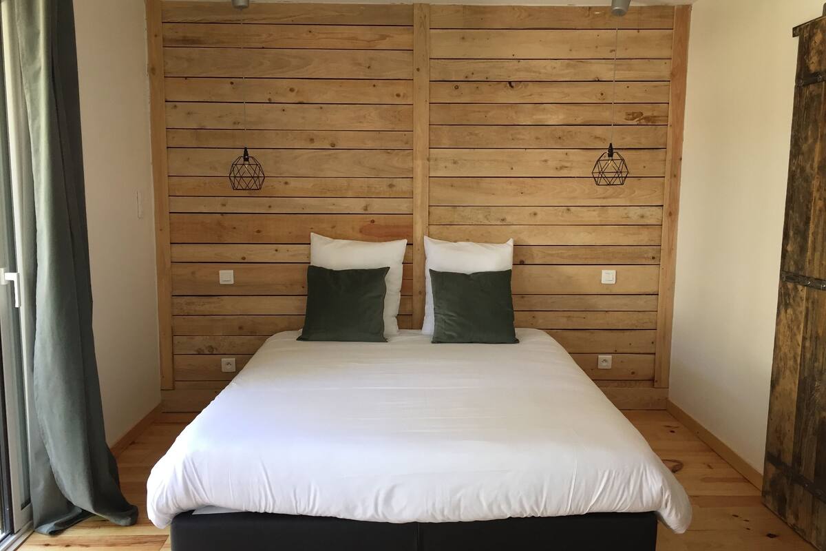 A bedroom with a wooden slat wall, a bed with white bedding, two green pillows, and two wall-mounted light fixtures.