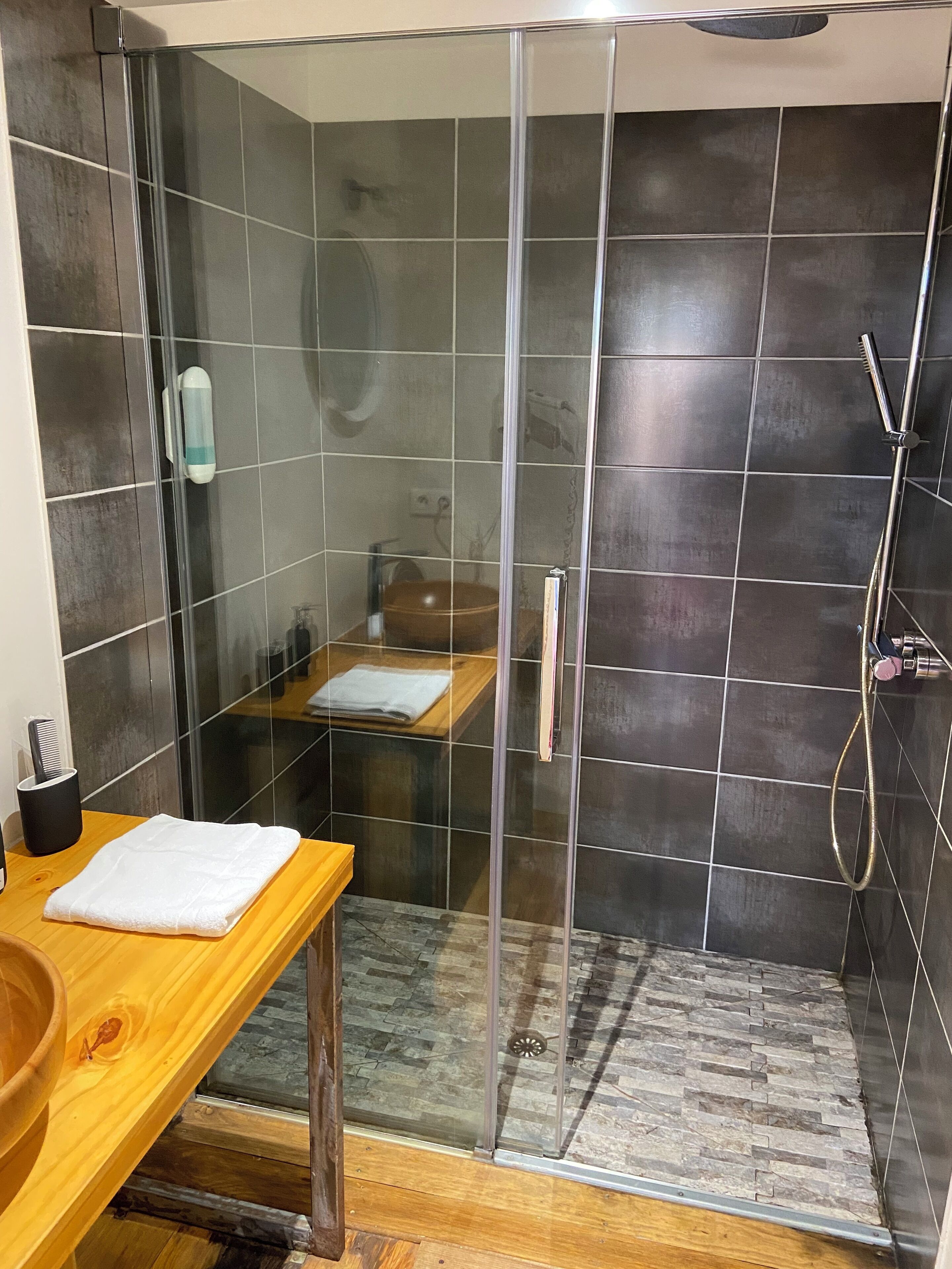 A modern bathroom with a glass shower enclosure, a wooden vanity, and a towel on the counter.