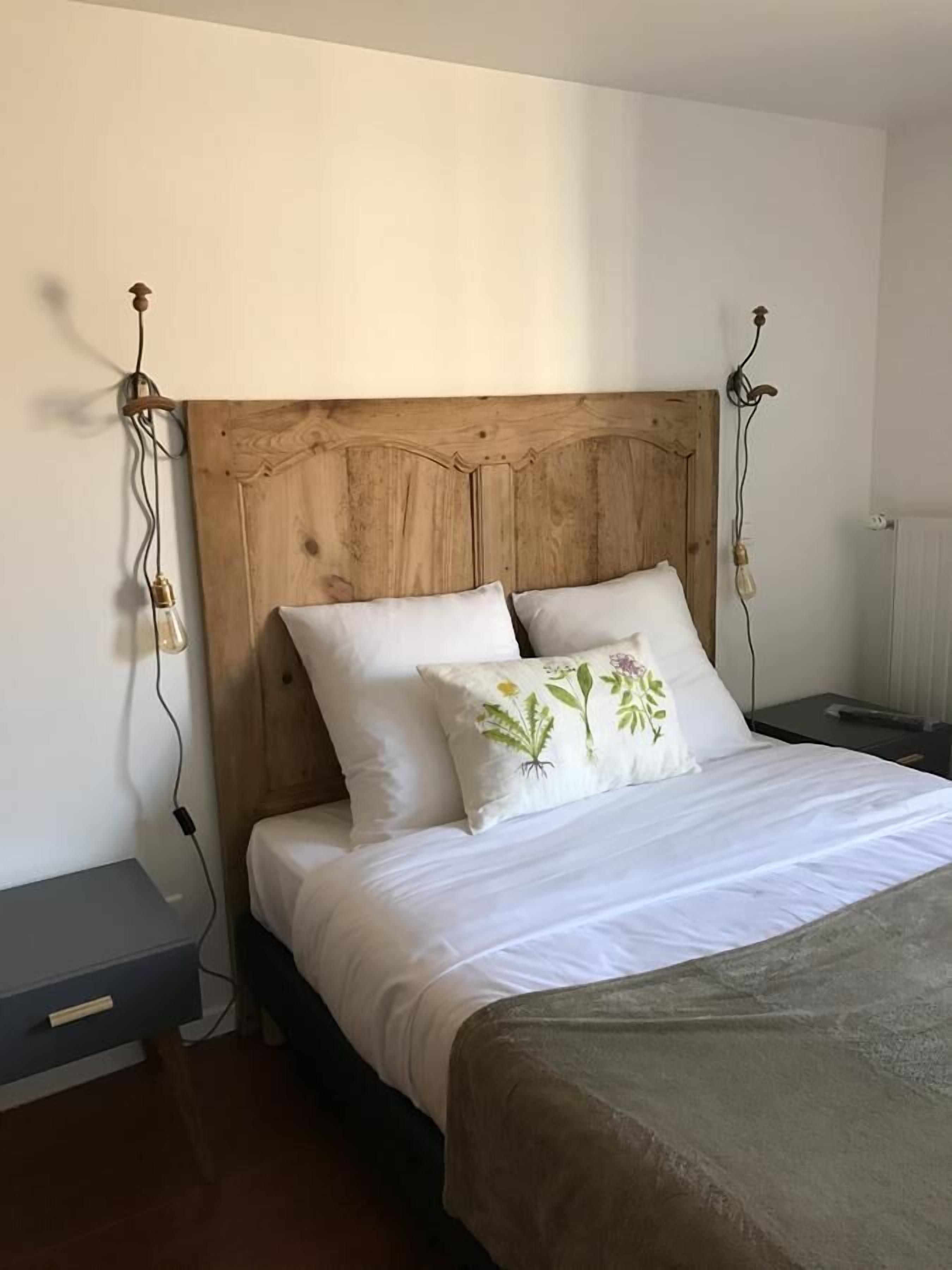Een bed met een houten hoofdbord, witte beddengoed en een sierkussen met bloemen.