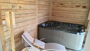 Uma cabana de madeira com uma banheira de hidromassagem, uma poltrona de descanso e uma pequena mesa com uma xícara.