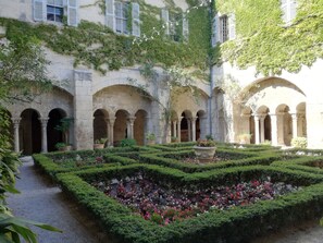 A courtyard with stone arches, a central flower bed, and potted plants.