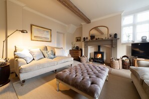A cozy living room with a sofa, ottoman, fireplace, and television.