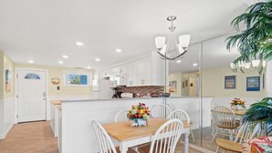Une cuisine moderne avec des meubles blancs, un îlot central en bois et un coin repas avec des chaises blanches.