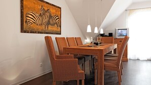 A dining area with a wooden table and wicker chairs, a painting of zebras on the wall, and a television in the background. - Designer apartment Sommerloft, over 2 floors, welcomes you warmly! (Insel Poel / OT Schwarzer Busch)