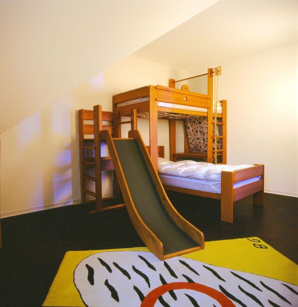 A bunk bed with a slide attached to the side, a ladder, and a colorful mat on the floor.