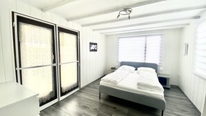 Un dormitorio con cama, mesita de noche, ventana con persianas y puerta con cortina estampada.