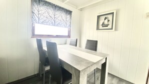 Un comedor con una mesa y sillas, una ventana con cortina de motivos de árbol y un cuadro en la pared.
