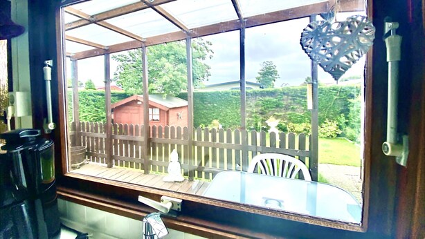 Una cocina con un amplio ventanal que da a una terraza de madera y un jardín cercado.