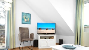 A living room with a TV on a white cabinet, a brown chair, and a white table with a blue bowl. - Apartment Südwind - Beachfront Holiday! (Insel Poel / OT Schwarzer Busch)