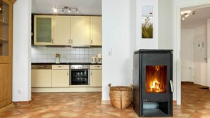 A modern kitchen with beige cabinets, a built-in oven, and a black wood-burning stove. - App. Wellenreiter is looking forward to your visit! (Insel Poel / OT Schwarzer Busch)