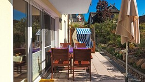 A patio with a table and chairs, a striped umbrella, and a glass door leading to a garden. - App. Wellenreiter is looking forward to your visit! (Insel Poel / OT Schwarzer Busch)