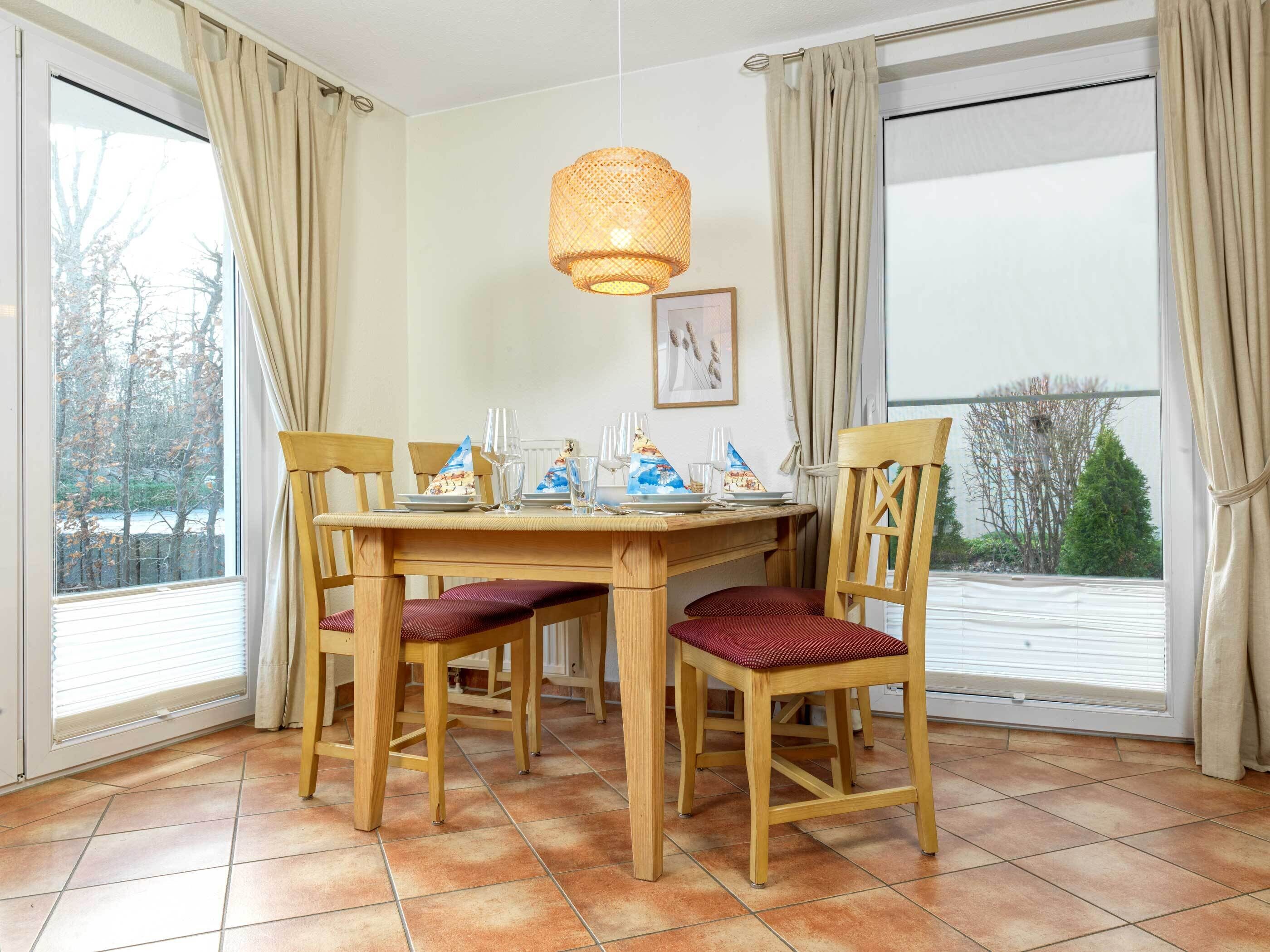Ein Essbereich mit Holztisch und Stühlen, einer hängenden Leuchte und Blick durch große Fenster.