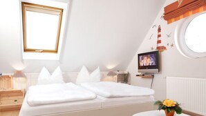 Une chambre moderne avec un lit, des tables de chevet, une télévision et une petite table ronde agrémentée d’un vase de fleurs.