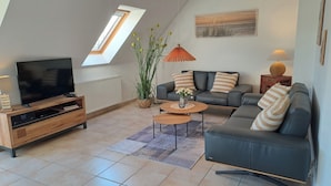 Un salon moderne avec un téléviseur à écran plat, un ensemble de canapés, une table basse et une plante en pot.