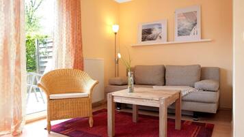 Una sala de estar acogedora con un sillón de mimbre, un sofá, una mesa de centro y una alfombra roja.