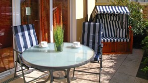 A patio with a round glass table, two striped chairs, and a striped umbrella. - App. Leuchtfeuer - Vacation right on the beach! (Insel Poel / OT Schwarzer Busch)