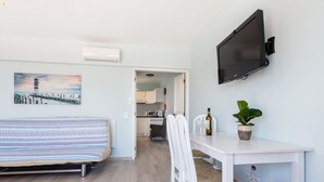 Ein modernes Wohnzimmer mit einer Couch, einem Esstisch mit Stühlen, einem an der Wand befestigten Fernseher und einem Topf mit Pflanze.
