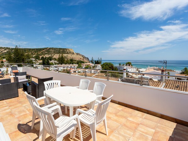 A terrace with a round table and chairs, overlooking a coastal town with buildings and a hill in the background. - Mariners (2) - Bright and stylish apartment - 2 minute walk to the beach (Luz)
