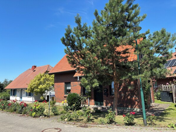A residential area with brick houses, a large pine tree, and a clear blue sky. - Hus an Diek - Cozy holiday home in a quiet location. (Insel Poel / OT Kaltenhof)
