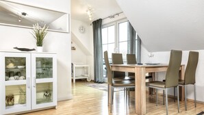 Ein moderner Essbereich mit Holztisch und -stühlen, einer Glasschrank mit Geschirr und einem Blick ins Freie durch große Fenster.