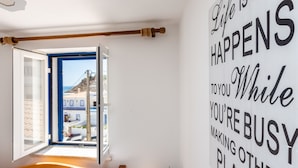 A bedroom with a large window, a bed, a bedside table with a lamp, and a wall with motivational text. - Casa Pedro - Burgau - Unique Converted Fisherman's Cottage (Budens)