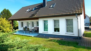 A modern house with a tiled roof, a covered patio, and a well-maintained lawn.