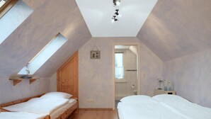 A bedroom with two wooden beds, a skylight, a wooden wardrobe, and a small bedside table with a lamp.
