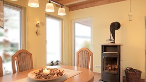 A cozy dining area with a wooden table, chairs, and a central decorative item. A fireplace with logs is visible in the background.