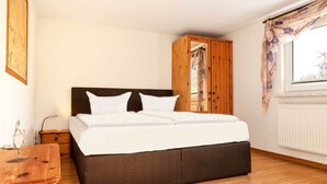 A bedroom with a bed, wooden wardrobe, bedside table, and a window with curtains. - Apt. Dwarslöper - Peaceful holiday apartment in Kirchdorf in the owner's house. (Insel Poel / OT Kirchdorf)