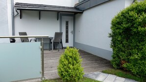 A small outdoor seating area with a table and chairs, a door, and a small bush. - Apt. Dwarslöper - Peaceful holiday apartment in Kirchdorf in the owner's house. (Insel Poel / OT Kirchdorf)