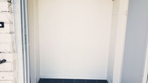 A room with a tiled floor, a door with a metal handle, and a black shelf with hooks. - StayPlus Central Apartment With Garden (Kristiansand)