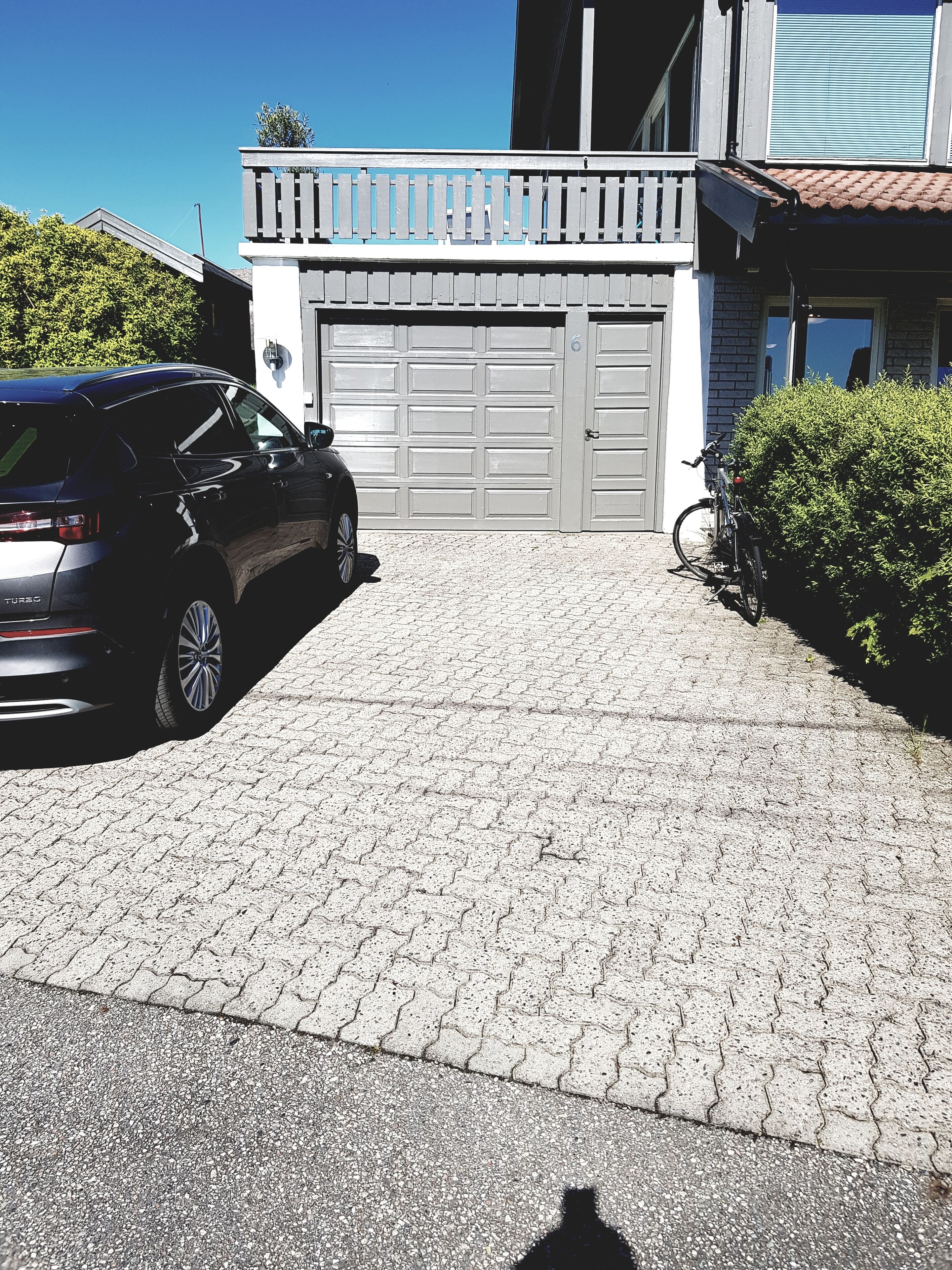 Une allée pavée mène à un garage où une voiture est garée sur le côté gauche.