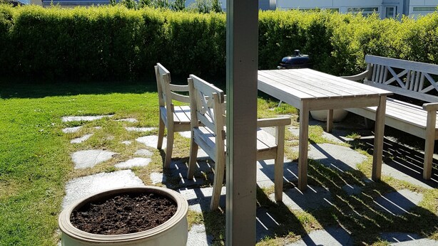 A patio area with a table and chairs, a large planter, and a metal mug. - StayPlus Central Apartment With Garden (Kristiansand)