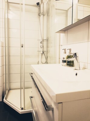 A modern bathroom with a glass-enclosed shower, a white sink with a soap dispenser, and a mirror above the sink.