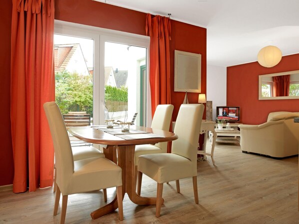 A dining area with a round table and four chairs, a sofa, a TV, and a lamp.